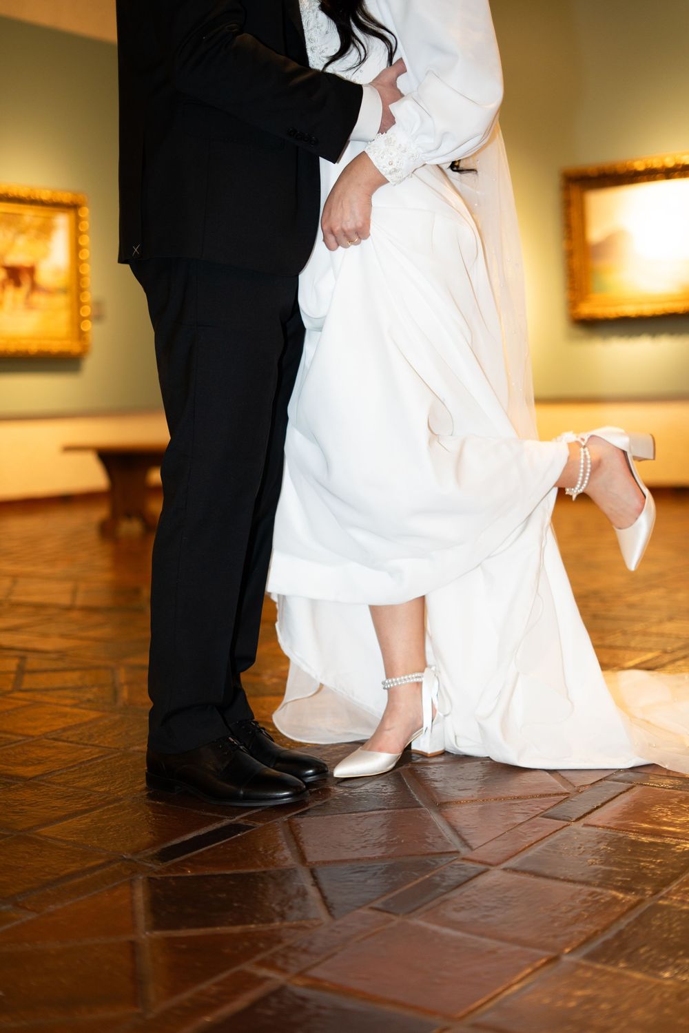 Bride in white gown and heels standing beside groom in black suit