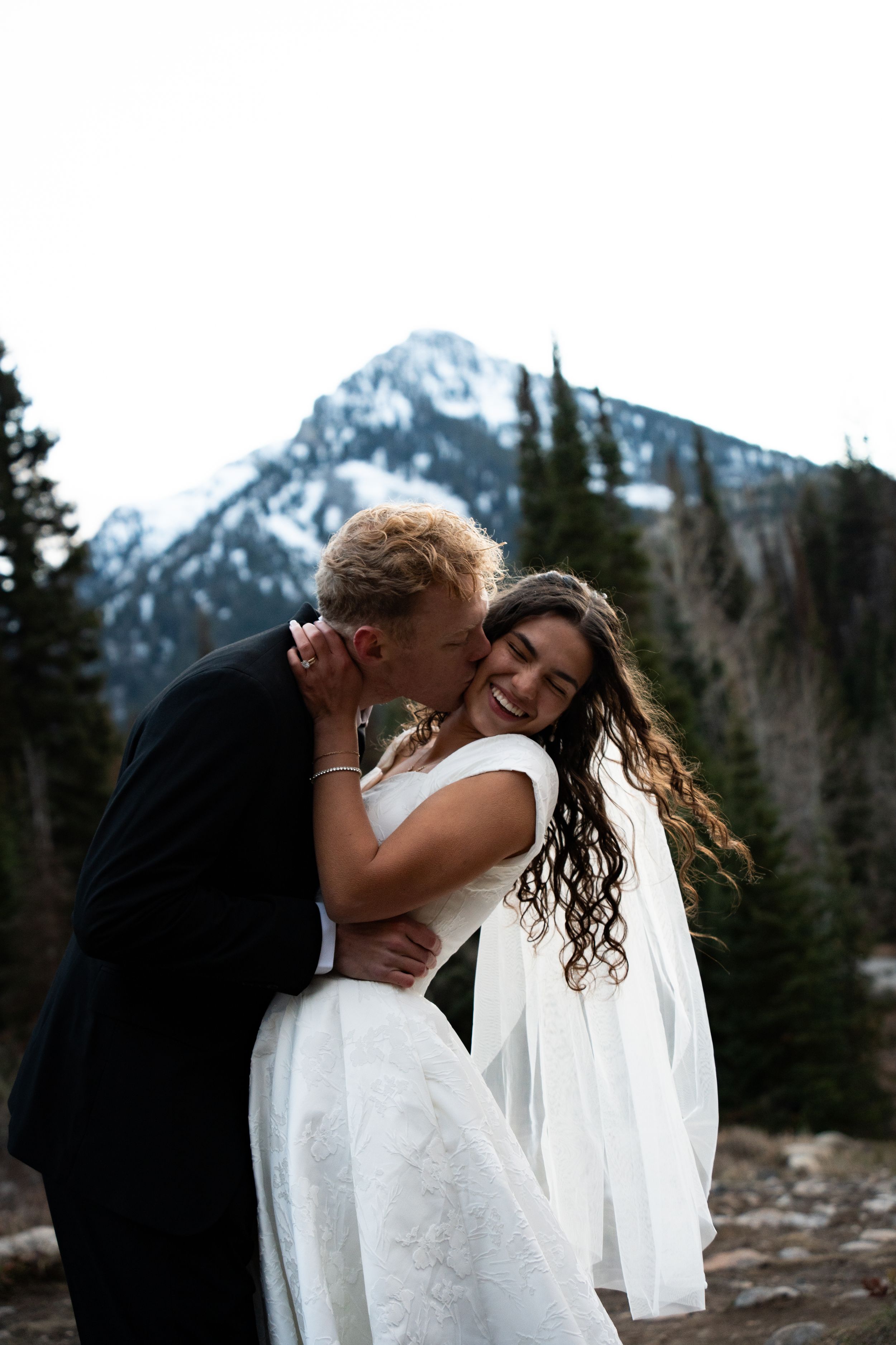 Groom kissing laughing bride during snowy winter bridal portraits at Brighton in the Wasatch mountains above Salt Lake City