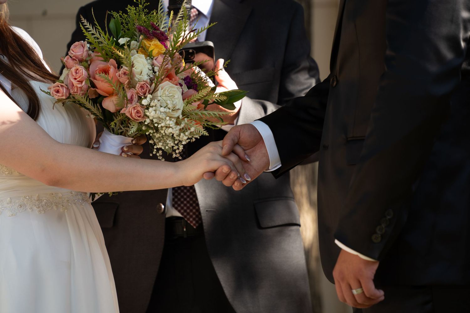 Bride and Groom holding hands during intimate summer backyard ceremony in Orem Utah. Bride holding a colorful bridal bouquet